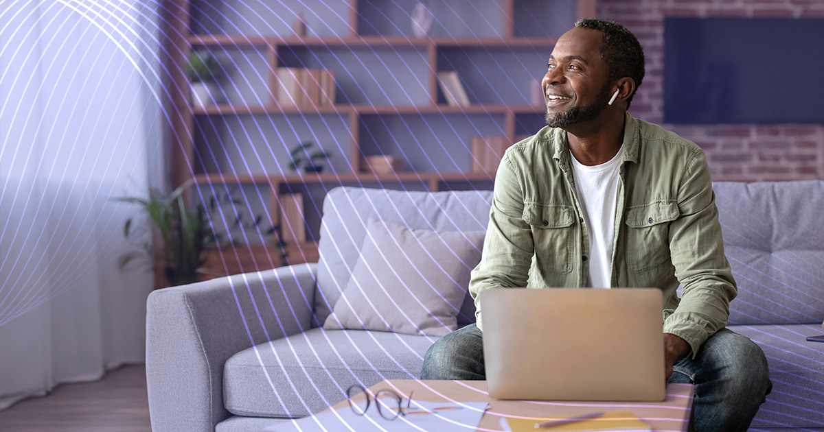 An educator sits at his laptop, earbuds in his ears