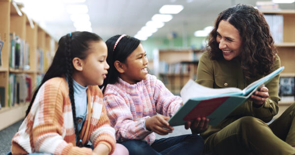 Teacher reading to two students in a library