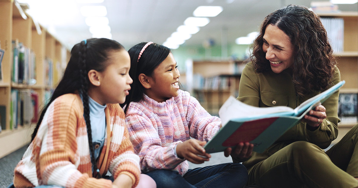 Teacher reading to two students in a library
