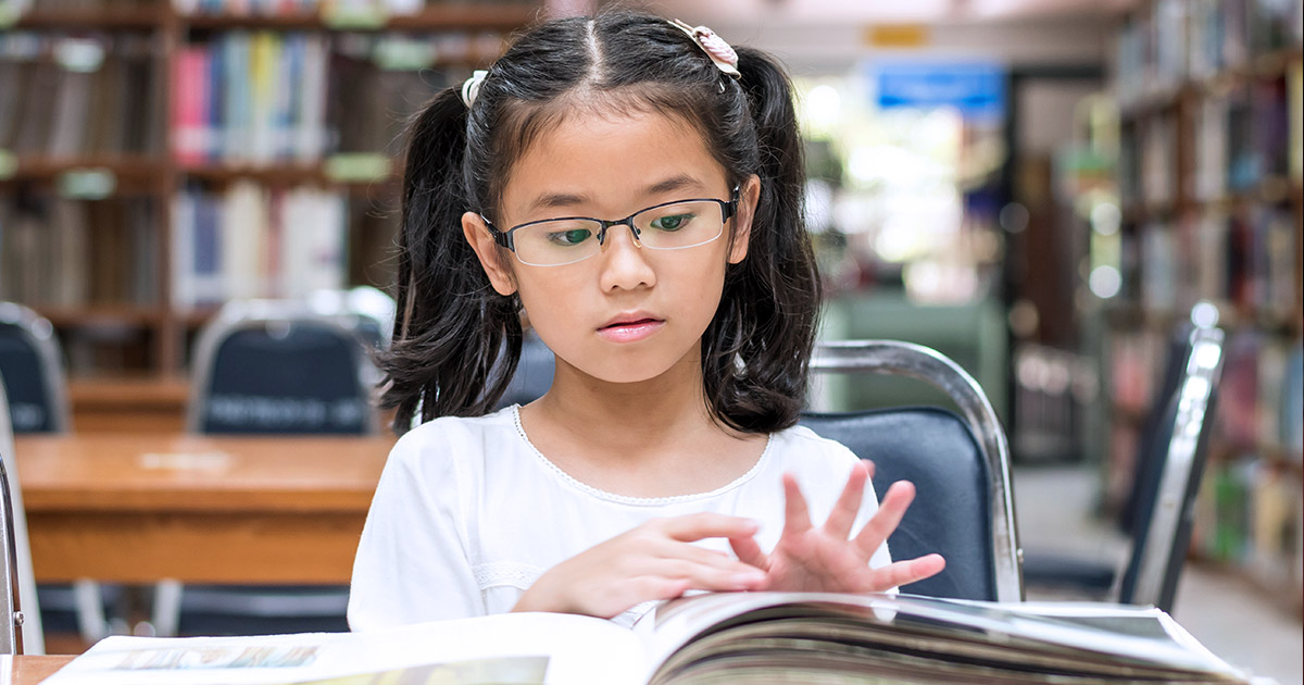 An elementary school student sitting at a table, flipping through a book