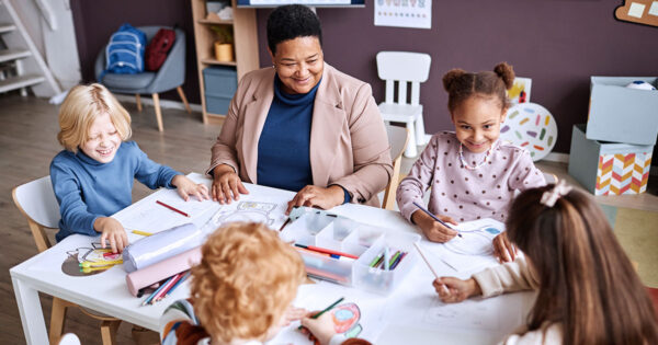 A teacher working with a group of early learners, all seated at a table