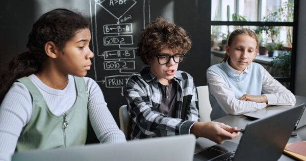 Three students in science class, sitting at a table with laptops