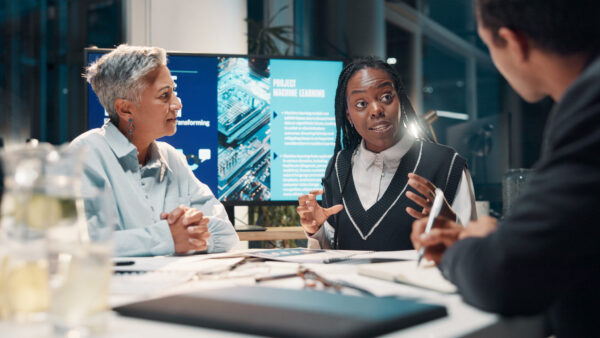 Three educators working at table with monitor in background
