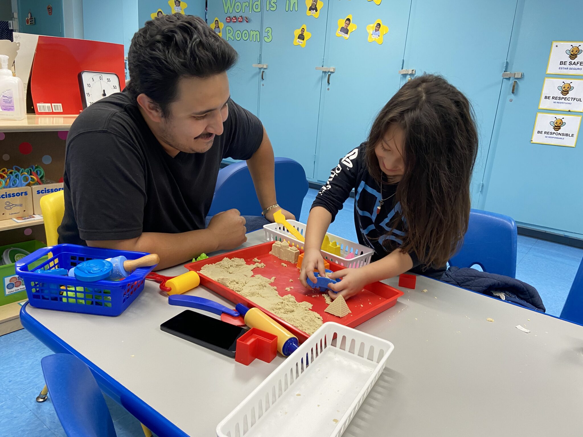 A child makes shapes out of play-doh in a classroom next to an educator.